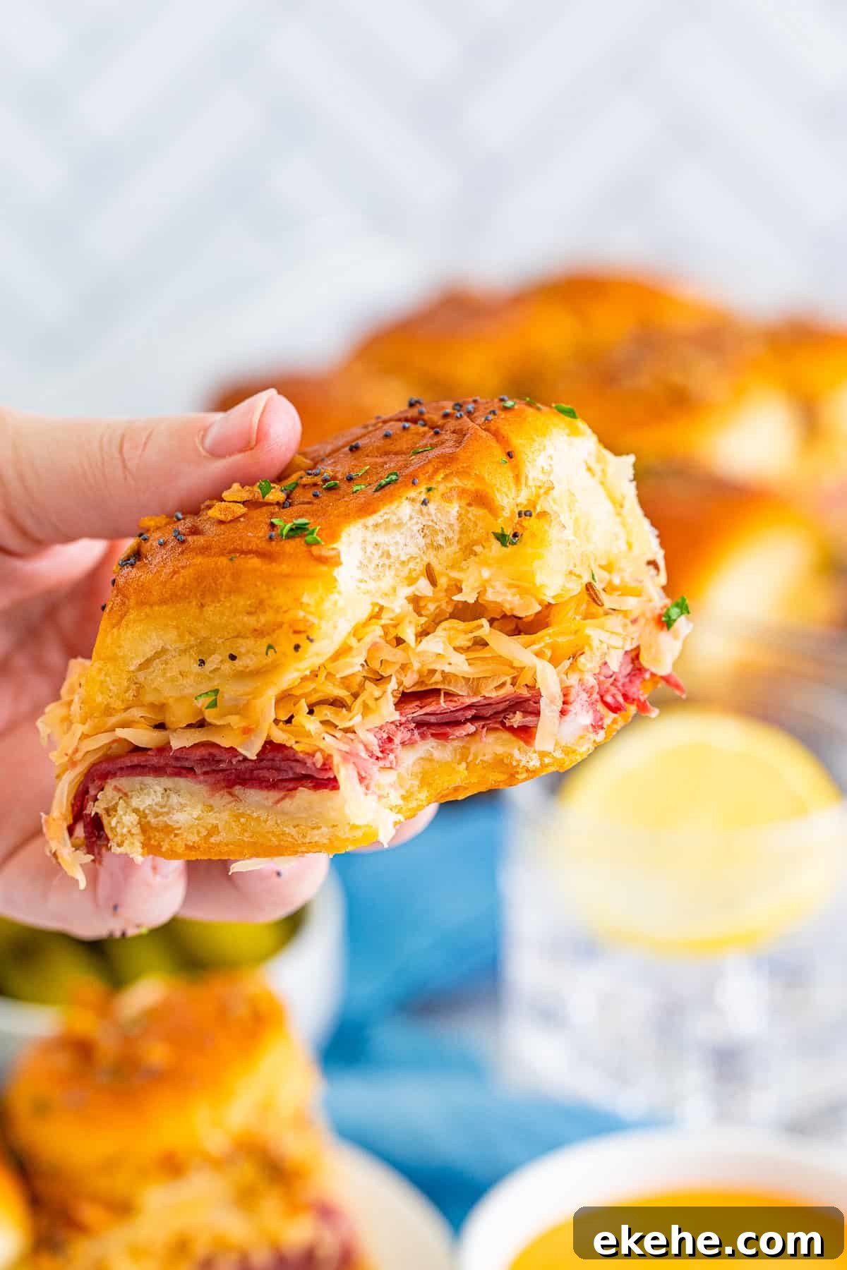 Hand holding up one Reuben Slider with bite taken out.