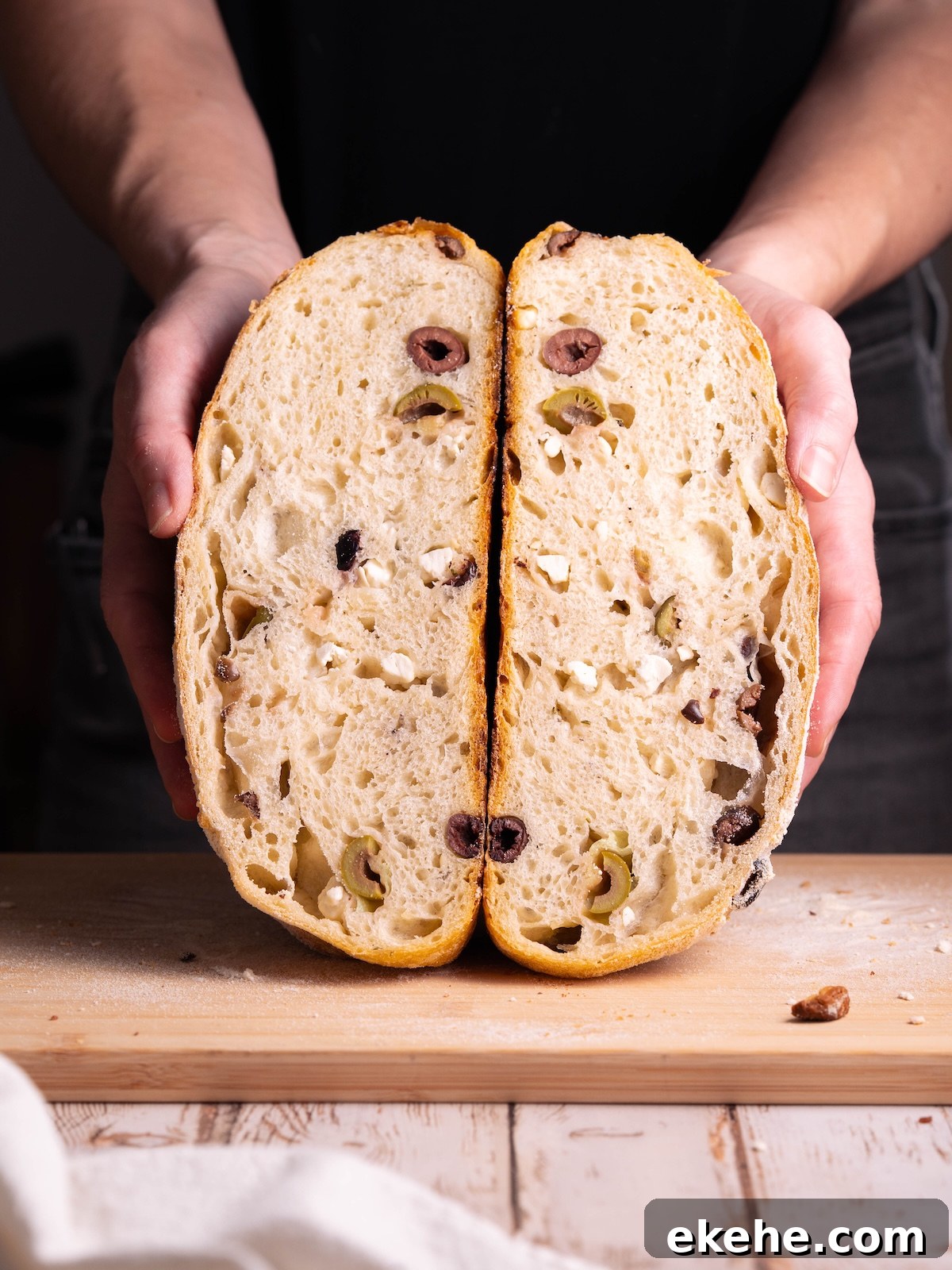 A loaf of sourdough sliced in half, showing olives and feta inside