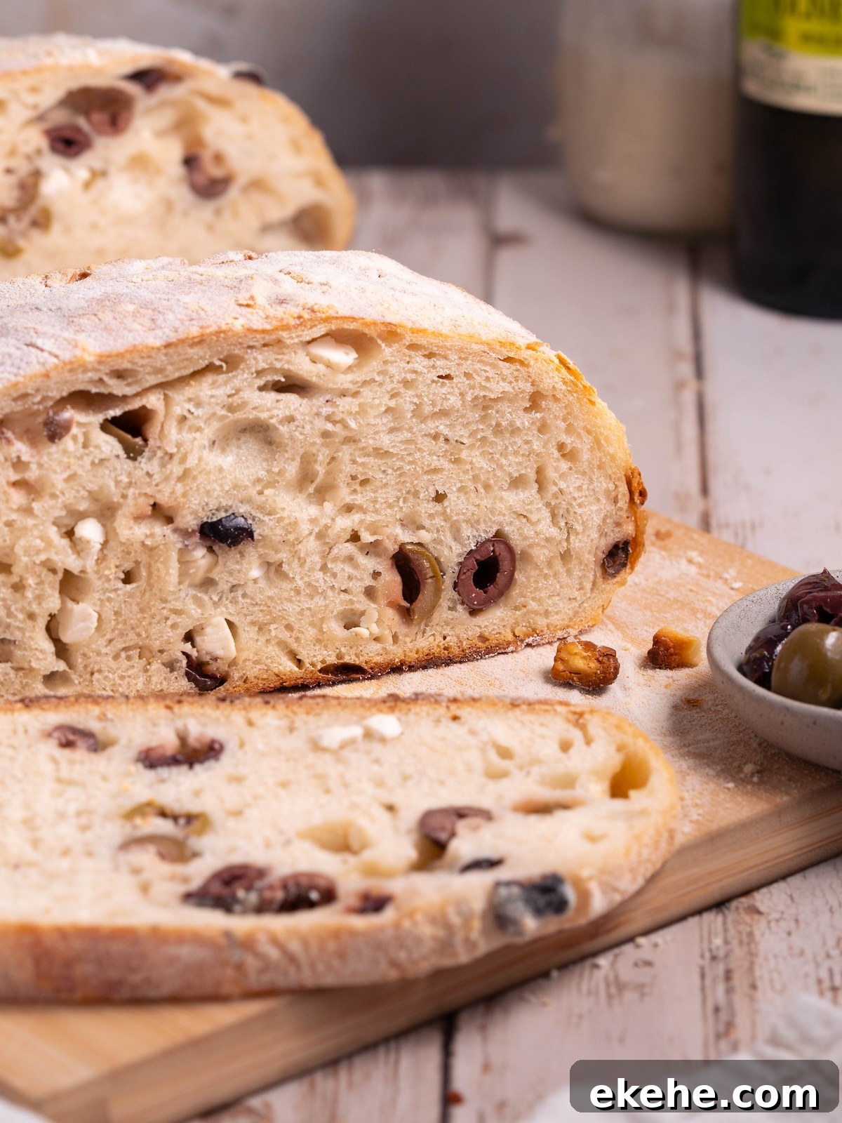A loaf of olive sourdough sliced on a wooden board
