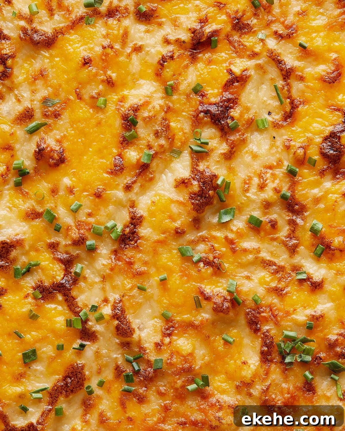 Up close and overhead image of cheesy mashed potatoes with garnish. 