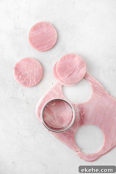 Sliced ham being cut into circles with a round cookie cutter.