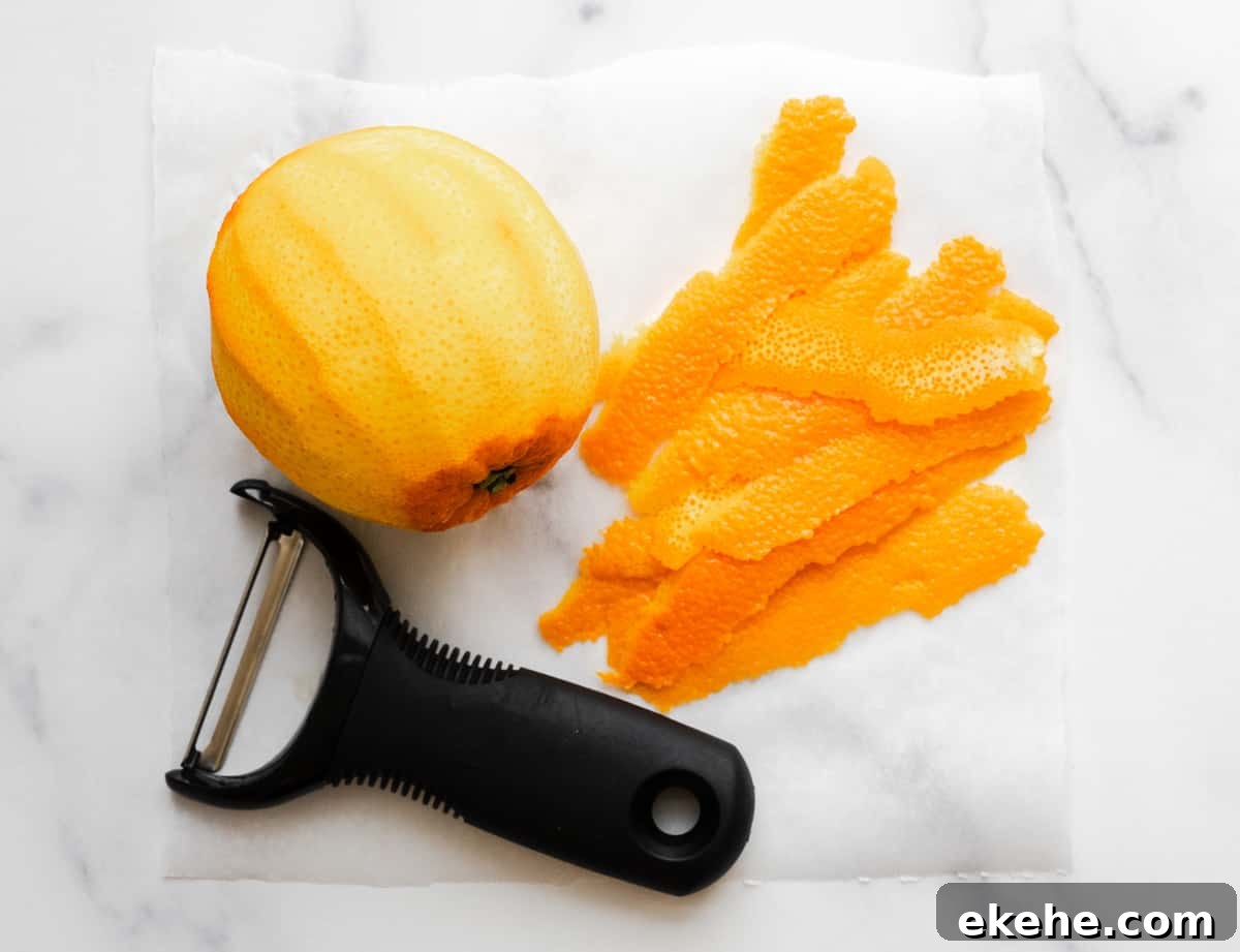 zested orange and zest with peeler on a marble board.