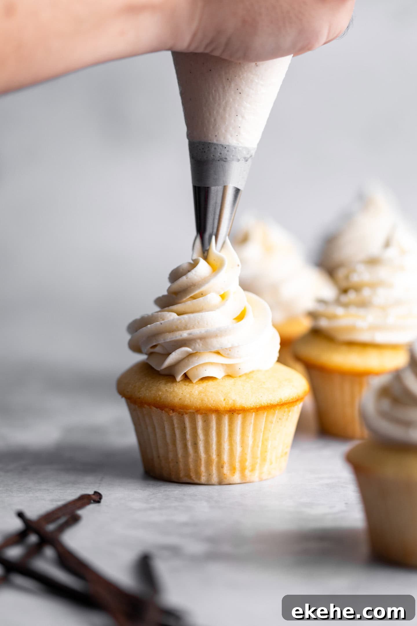 Double vanilla buttercream being piped on top of vanilla bean cupcake.