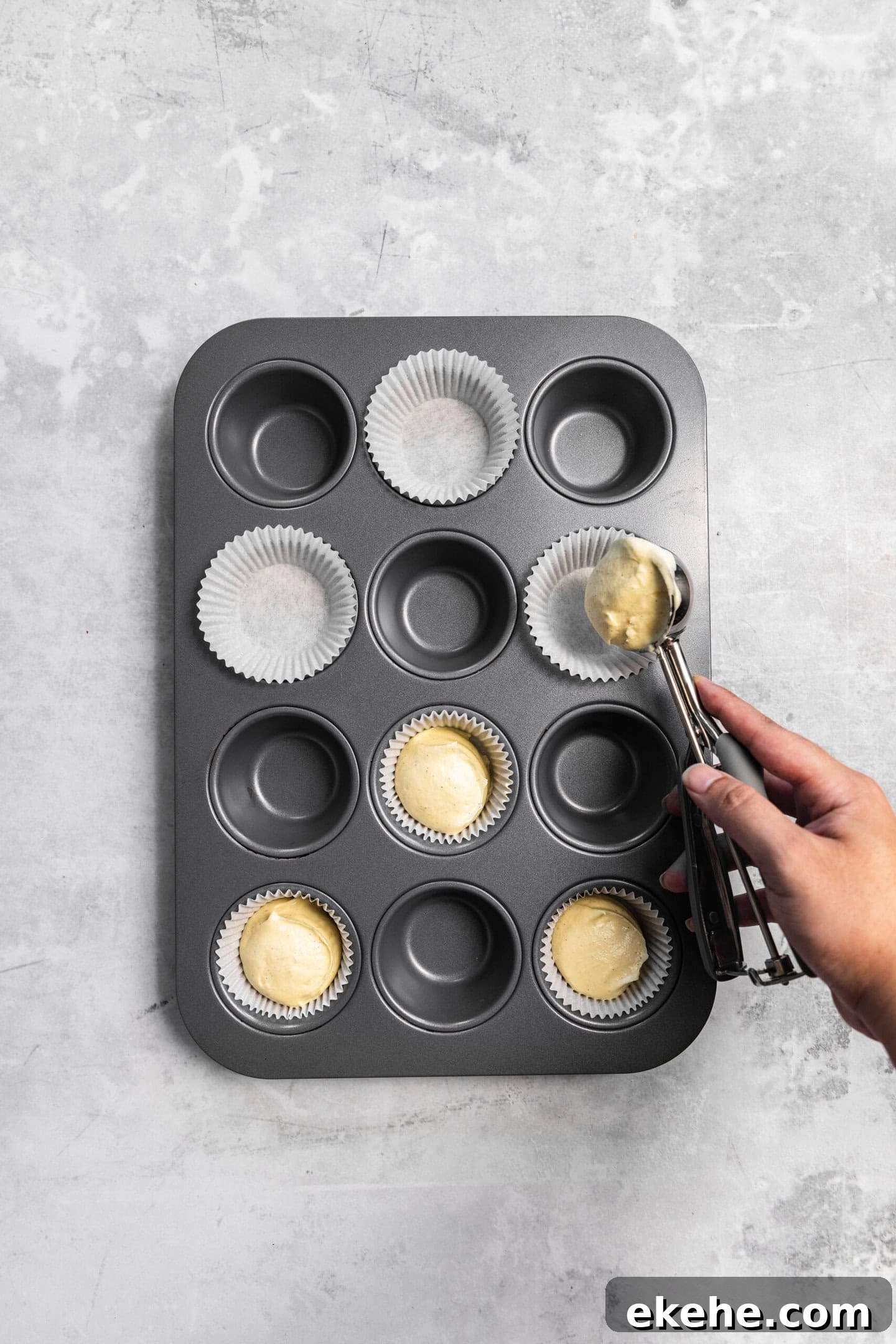 Cupcake batter being scooped into prepared muffin pan.