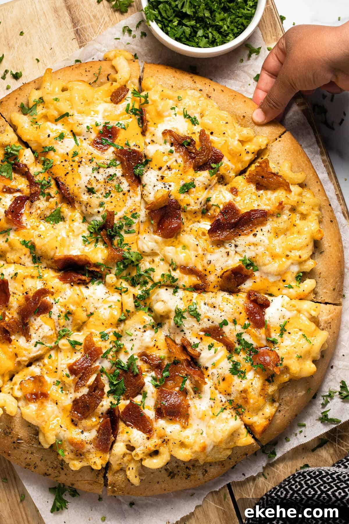 A hand reaching for a slice of mac and cheese pizza with bacon