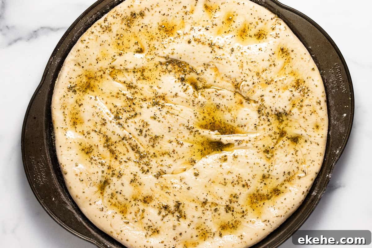 Pizza crust on a pizza pan with a layer of olive oil and herbs