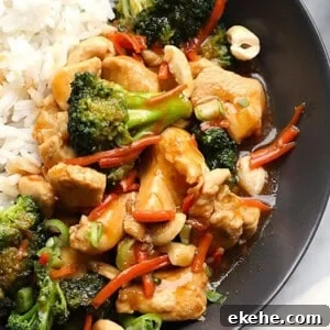 A plate with ginger chicken stir-fry, featuring broccoli, carrots, and cashews next to white rice.