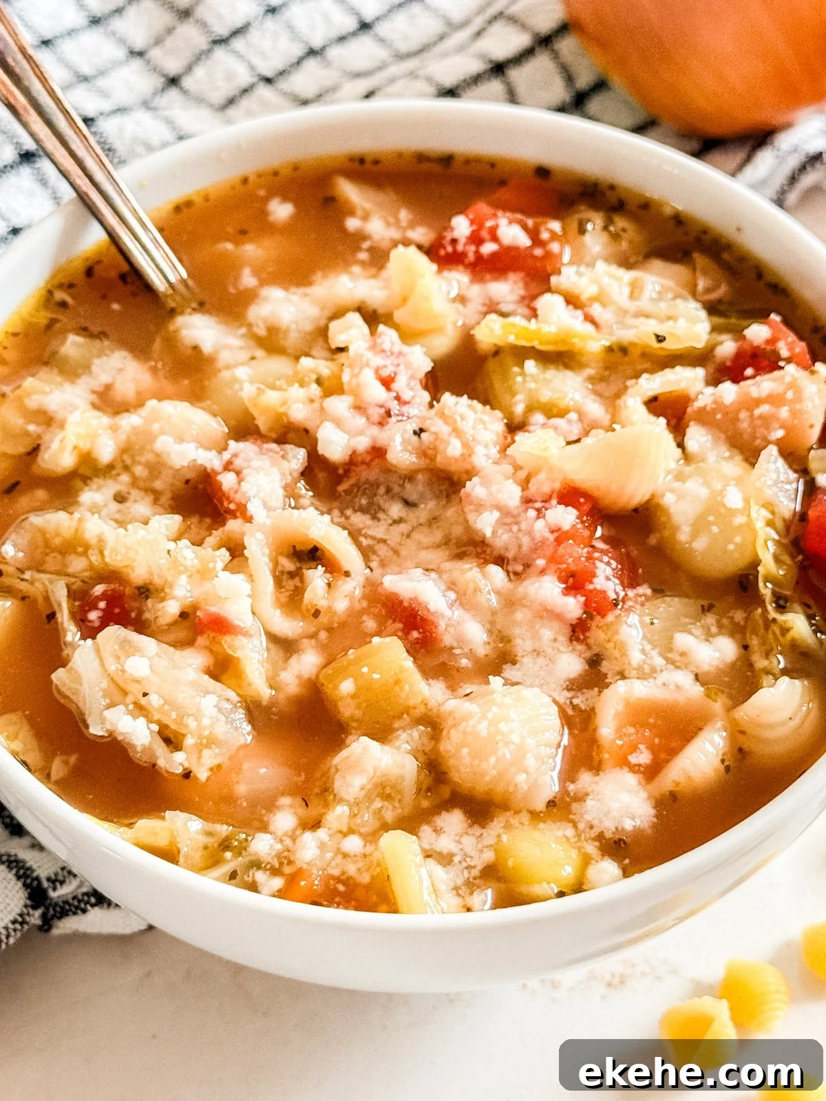 A close up image of a bowl of minestrone soup with a spoon in it.