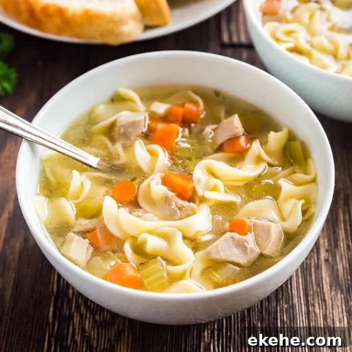 A bowl of chicken and egg noodles soup with sliced bread and another bowl behind it.