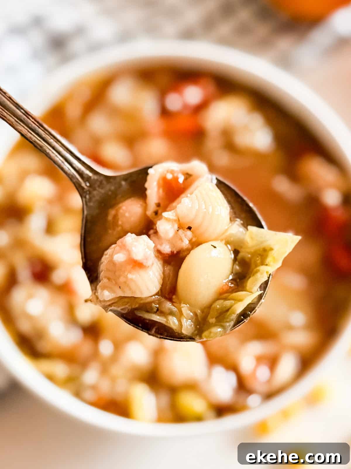 A close up of a spoon holding a scoop of minestrone soup.