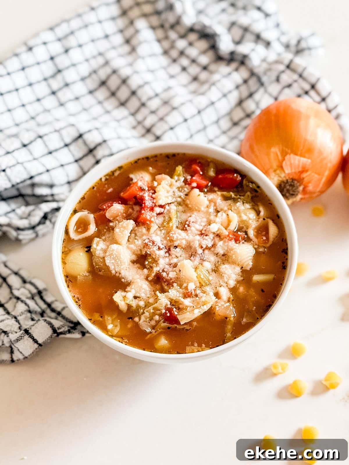 A bowl of traditional minestrone soup with a checked napkin and an onion behind it.