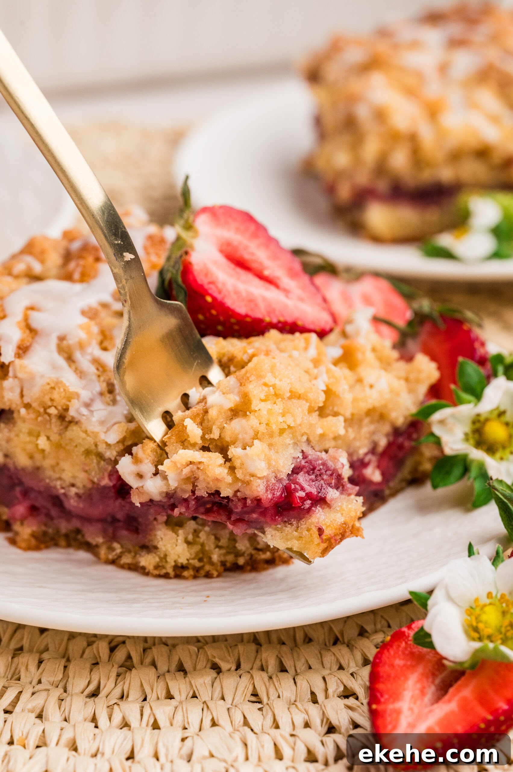 Strawberry Coffee Cake on a white plate with sliced strawberries with a fork taking out a bite