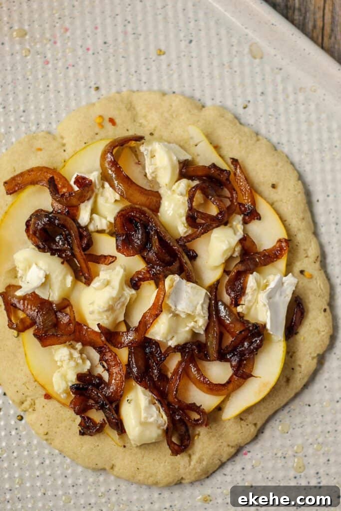 flatbread topped with pears, brie cheese and caramelized onion on a white baking sheet before being cooked
