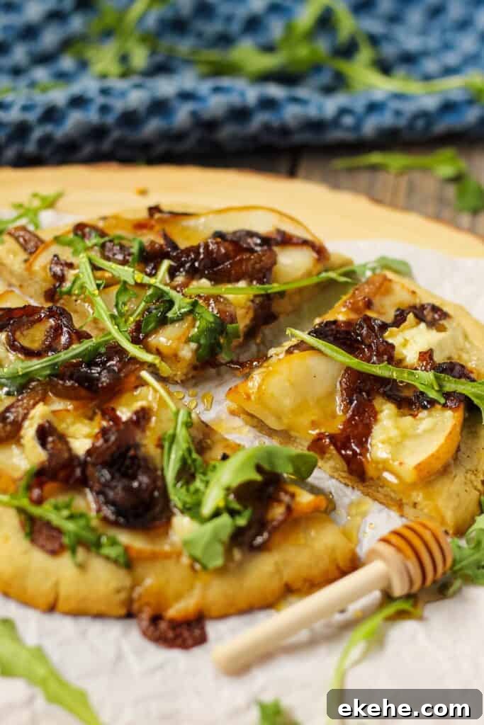 side shot of pear brie and caramelized onion topped flatbread on parchment on top of wooden serving board. garnished with honey drizzle and fresh arugula.