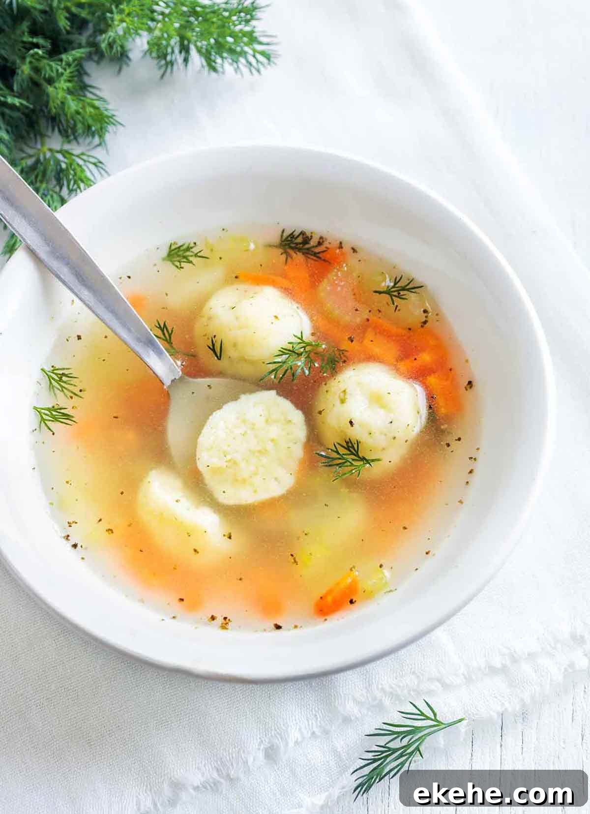 A white bowl filled with matzo ball soup and sprinkled with dill