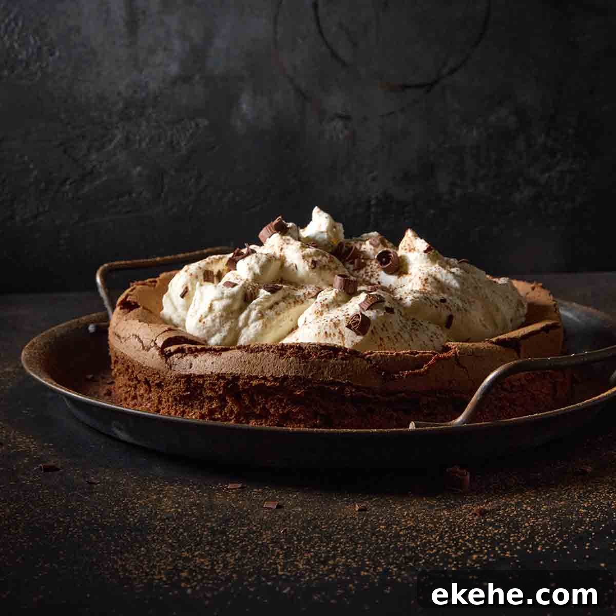 A flourless chocolate cloud cake topped with billows of whipped cream on a metal platter.