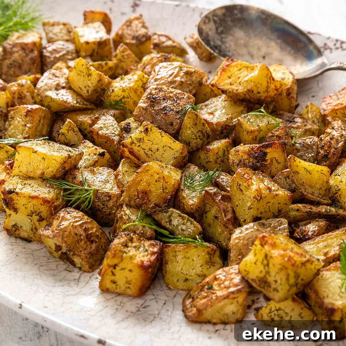 An oval platter filled with cubed roasted potatoes, garnished with fresh dill.