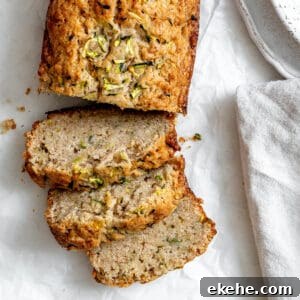 Slices of zucchini bread on white crinkled parchment paper. There's part of a speckled bowl in the top right corner, and part of a gray napkin in the bottom right corner.