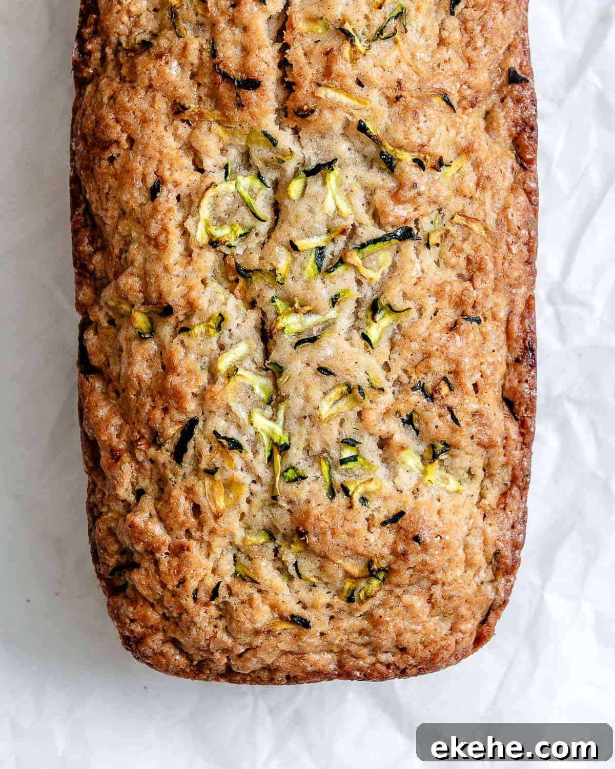 A freshly baked load of zucchini bread on top of a white crinkled parchment paper.