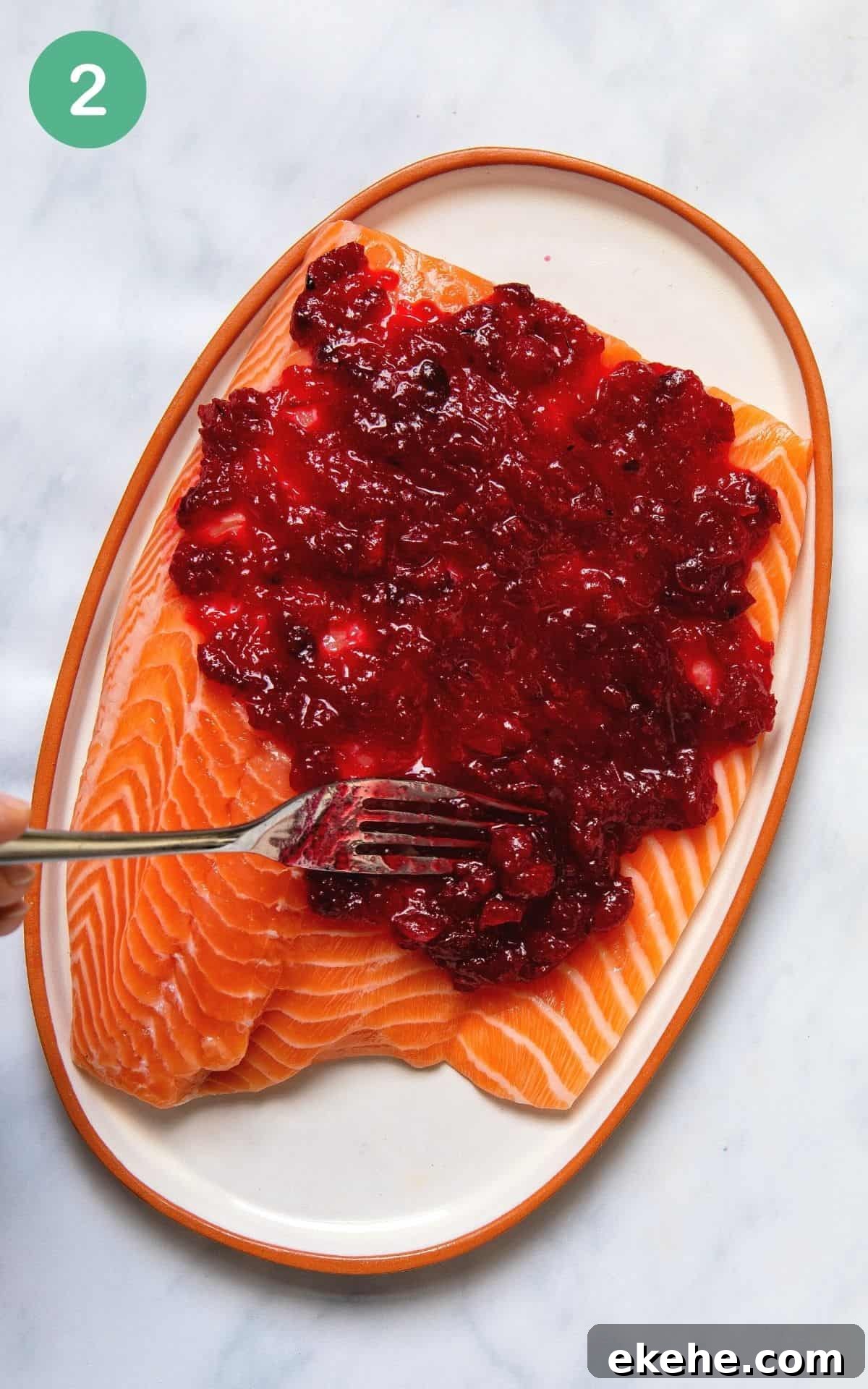 Spreading cranberry sauce with a fork onto a salmon fillet before baking.