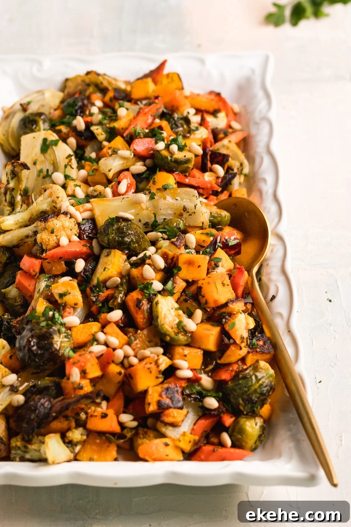 roasted veggies garnished with pine nuts on a white glass platter. 