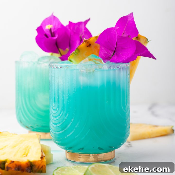 two glasses of a blue hawaiian cocktail garnished with pineapple wedges and flowers