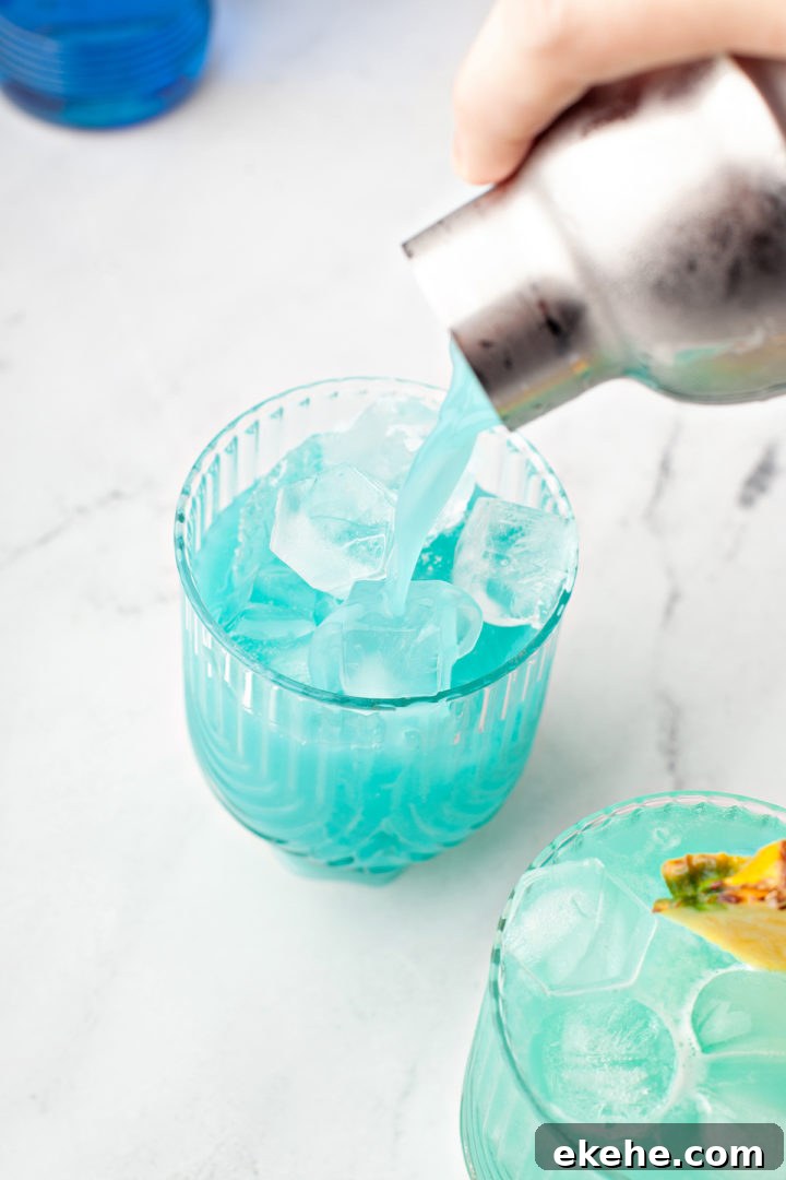 pouring a blue hawaiian cocktail out of a cocktail shaker into glasses of ice