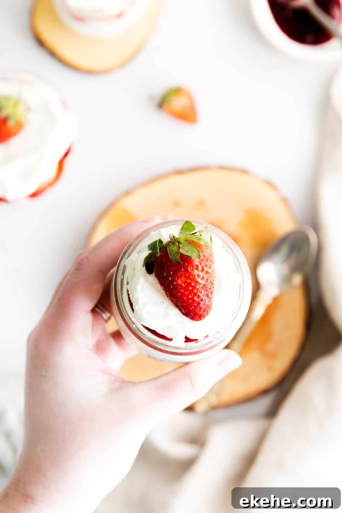 woman's hand holding small dessert cup topped with whipped cream and strawberry