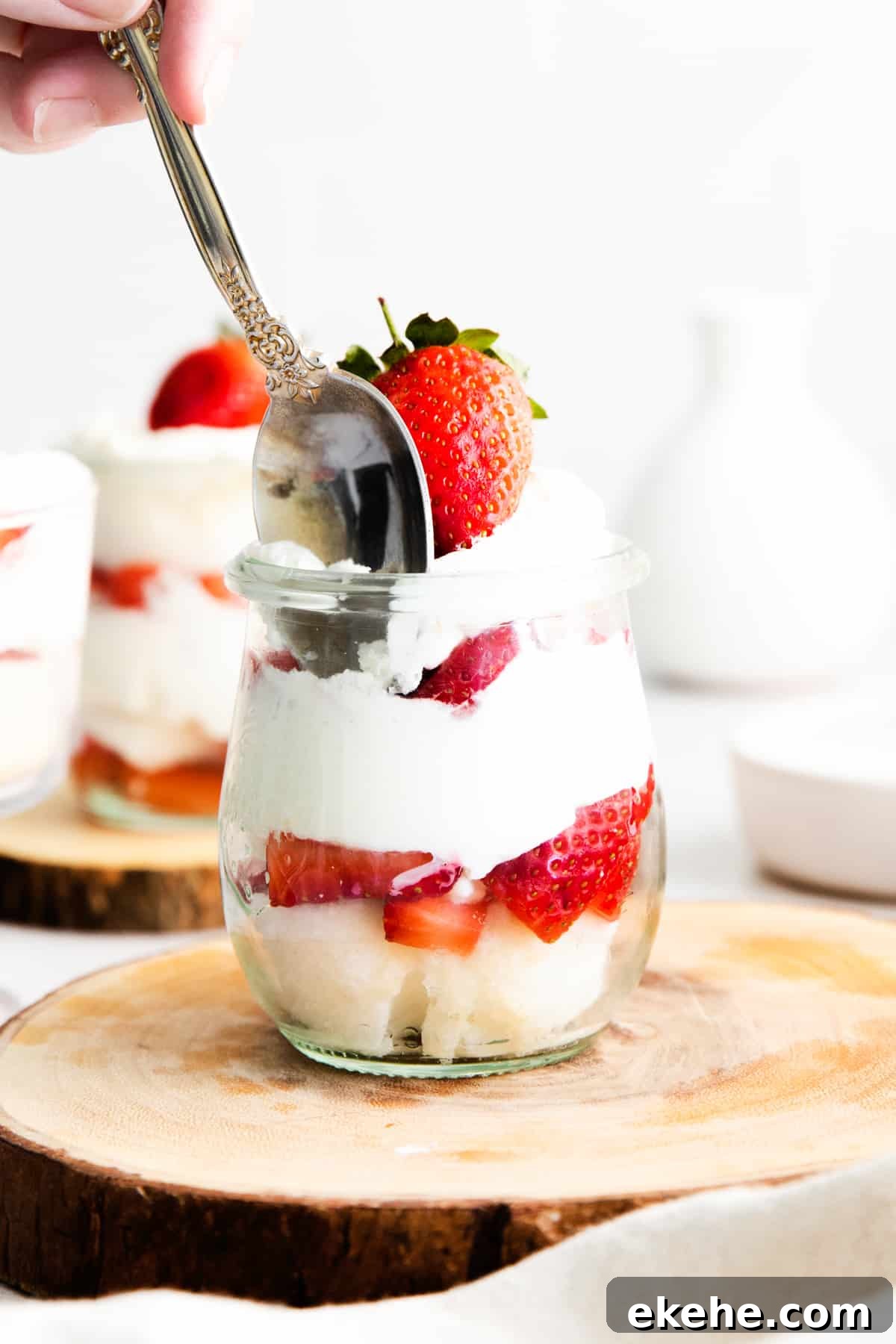 Spoon taking a scoop of whipped cream out of strawberry shortcake trifle