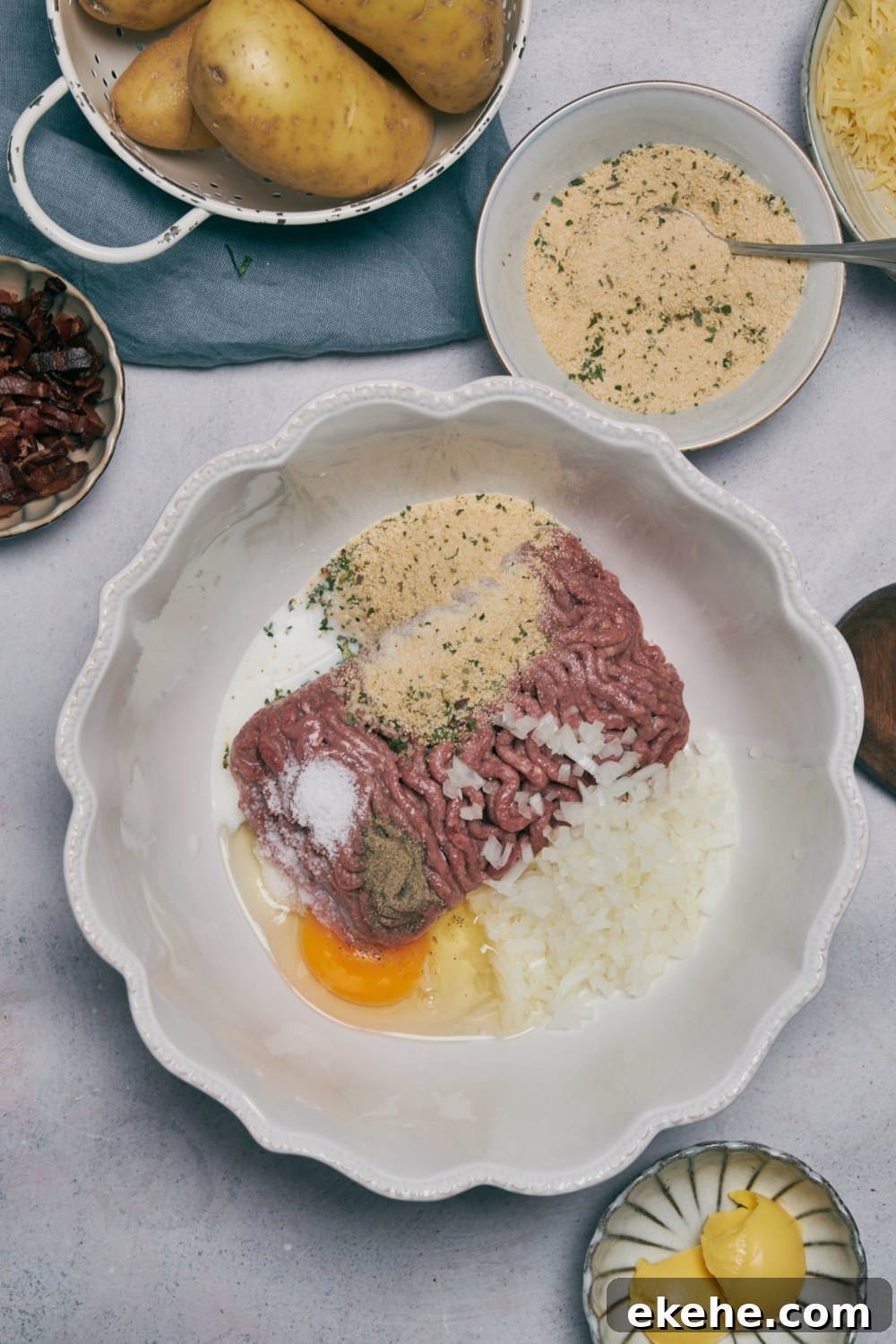 Ground meat, spices, a cracked egg, and onion in a white bowl.