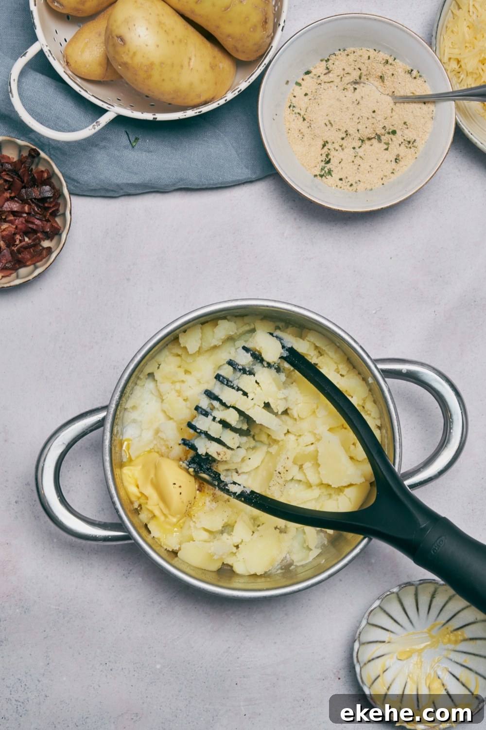 A potato masher and semi mashed potatoes in a silver cooking pot