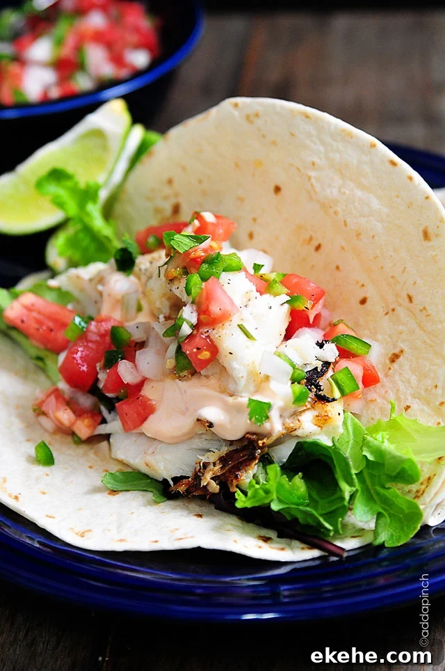 Fish taco topped with pico de gallo, salad greens and sriracha cream sauce, served on blue plate - addapinch.com