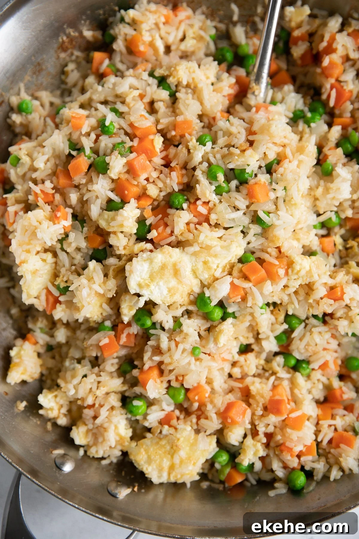 Large skillet filled with cooked fried rice made with cooked white rice, fried egg, onion, garlic, peas, and carrots.