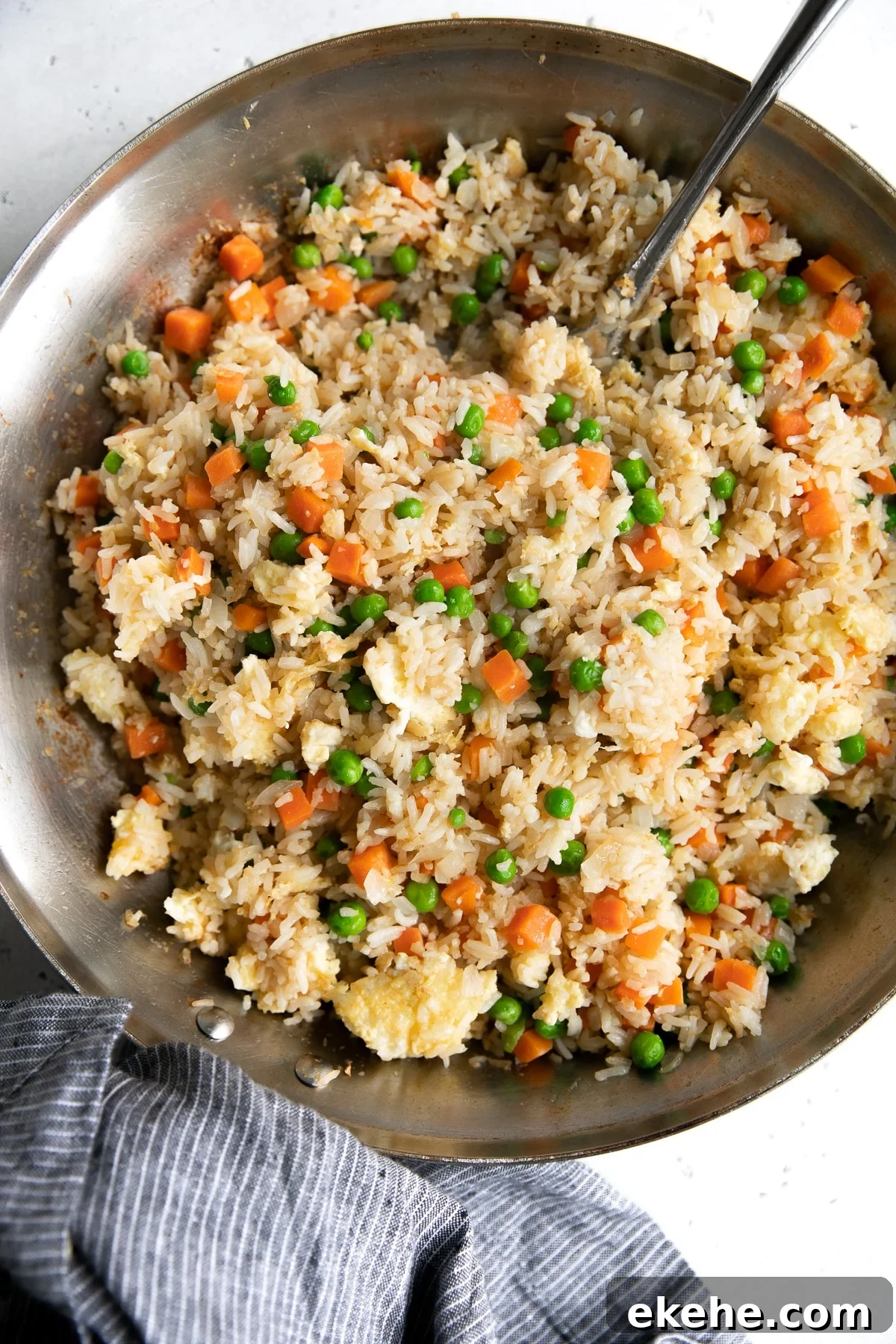 Overhead image of a large skillet filled with cooked fried rice made with cooked white rice, fried egg, onion, garlic, peas, and carrots.