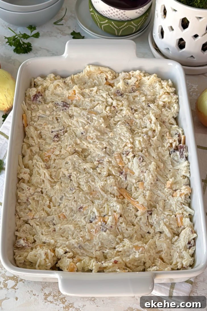 Unbaked hashbrown casserole mixture spread evenly in a white baking dish before going into the oven.