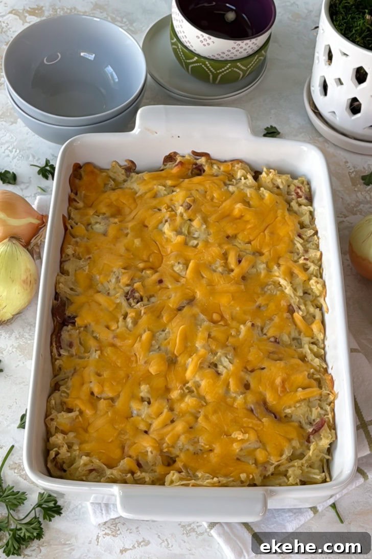 Baked hashbrown casserole in a white casserole dish with melted cheddar on top and golden edges.