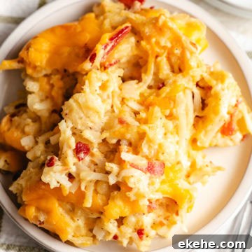 Close-up of a serving of hashbrown casserole on a white plate with melted cheddar and crispy potatoes.