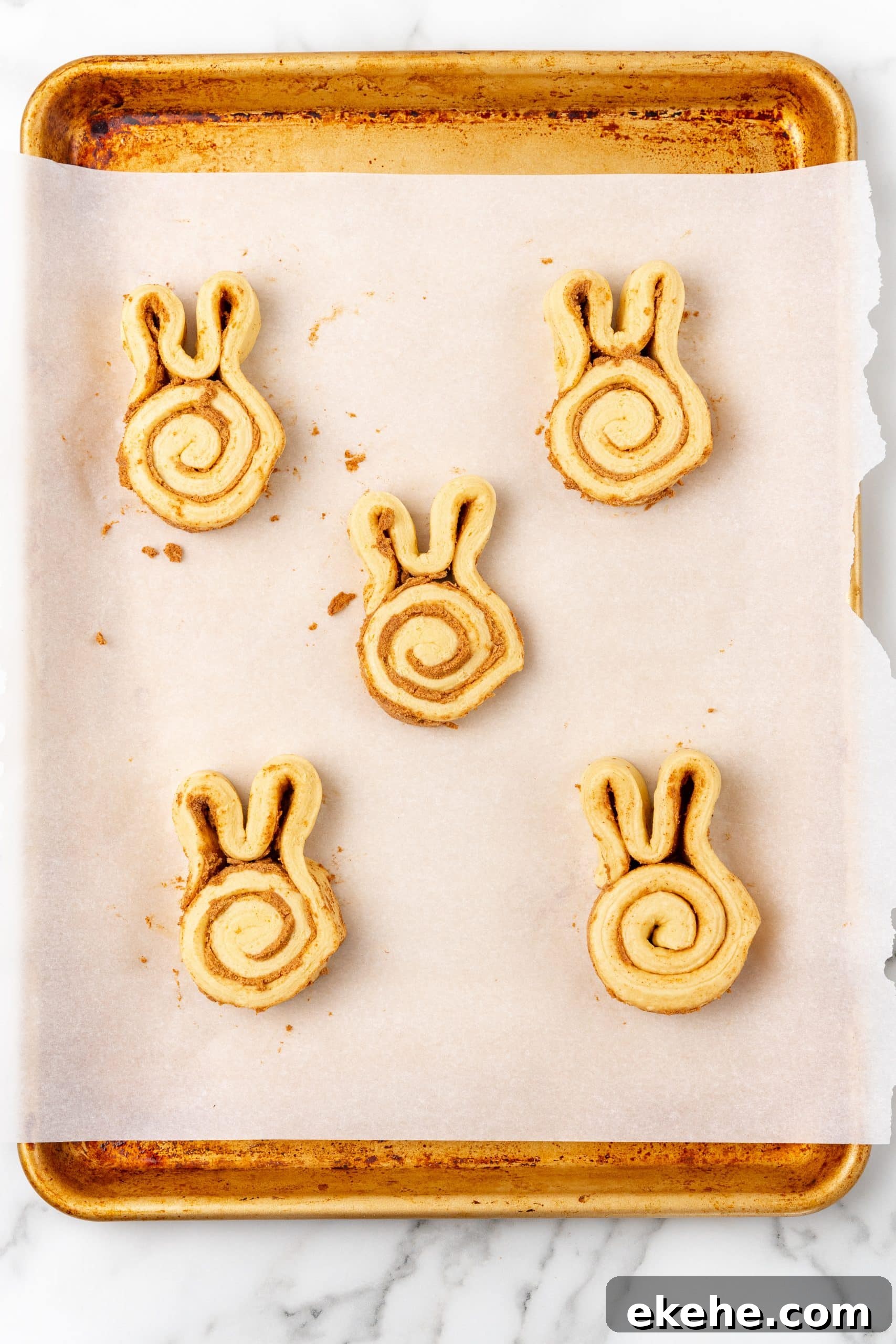 unbaked cinnamon bunny rolls on a parchment paper lined baking sheet