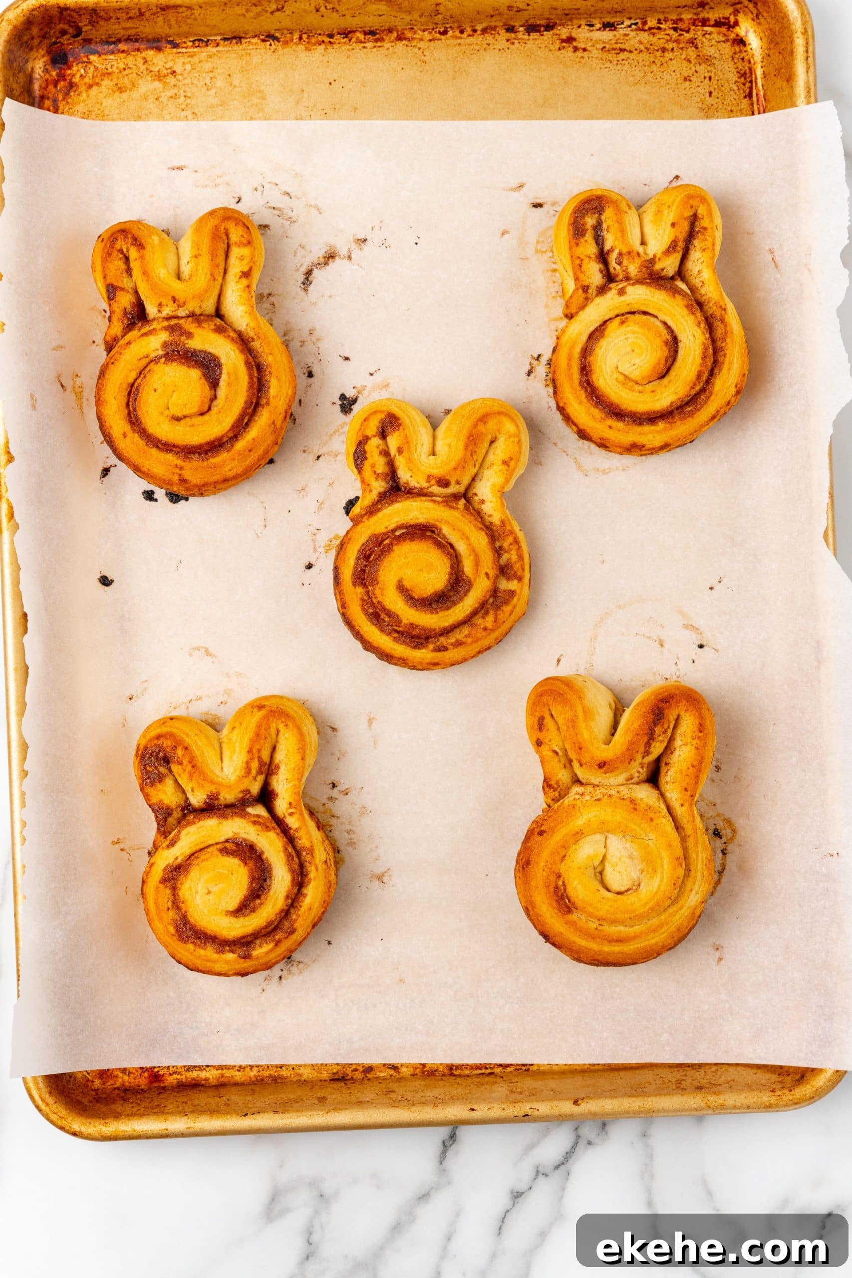 baked cinnamon bunny rolls on a parchment paper lined baking sheet
