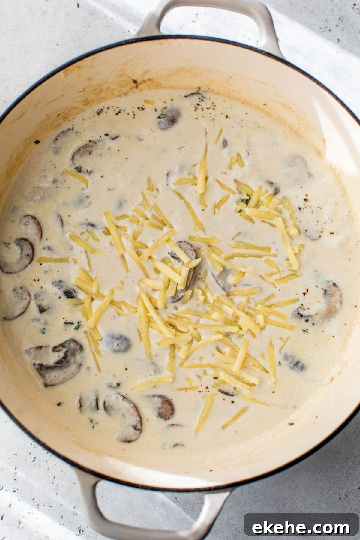 shredded cheese added to the dutch oven with cheese sauce and mushrooms