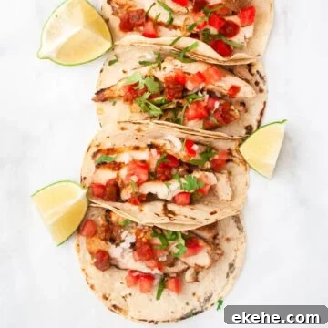 a top down view of a line of grilled chicken tacos surrounded by lime wedges.