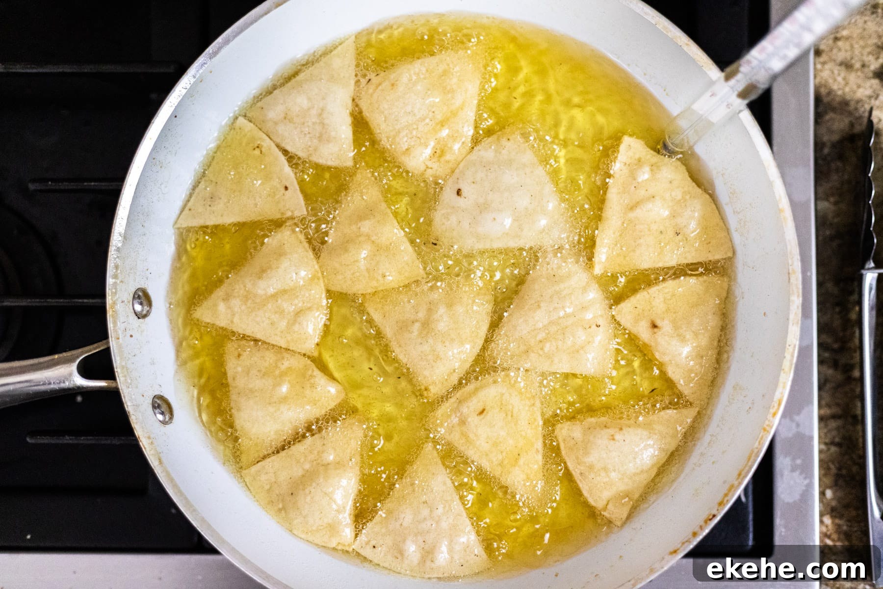 Corn tortilla chips frying in oil in a frying pan.