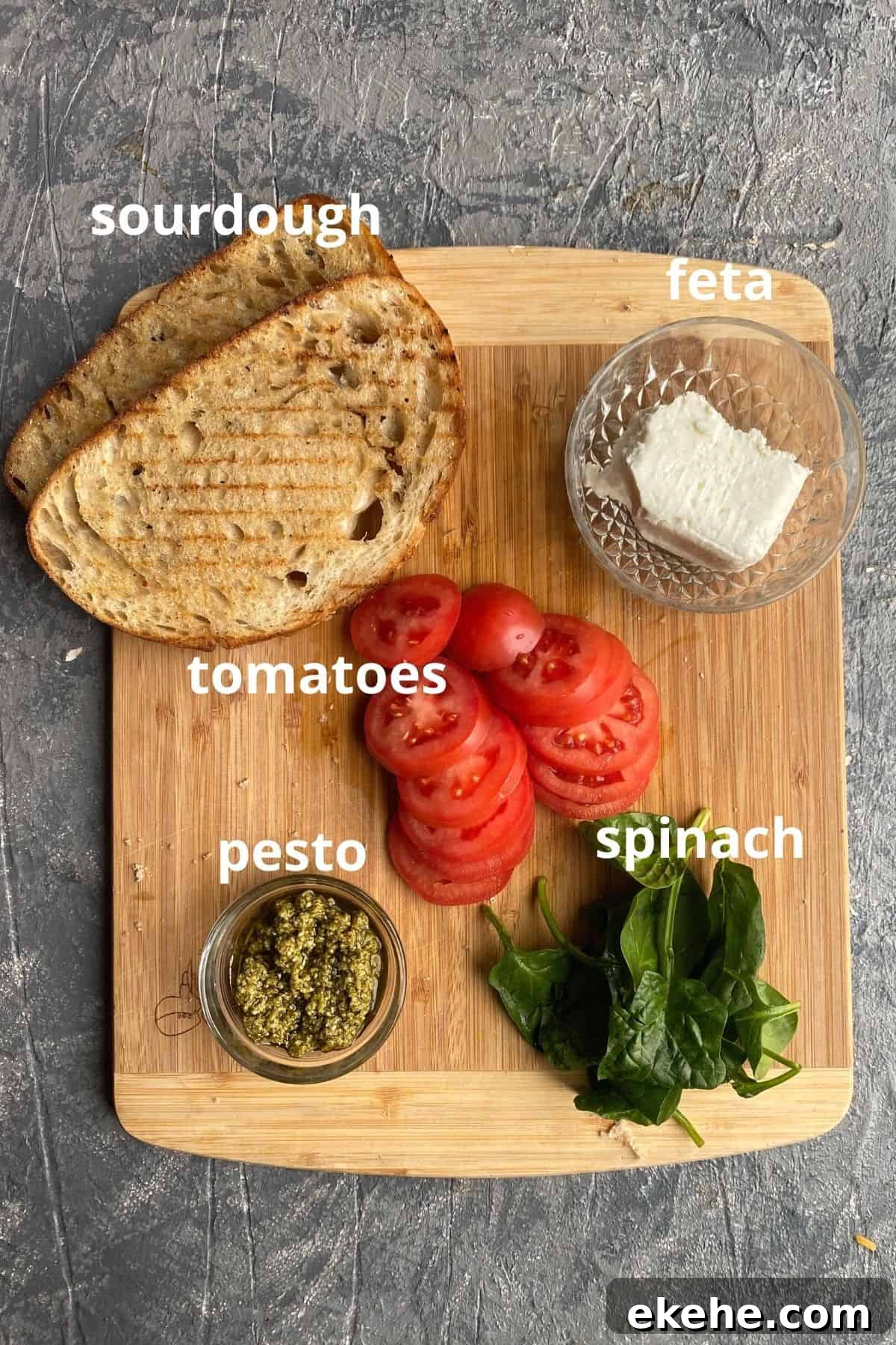 An overhead view of the ingredients to make a grilled cheese sandwich; sourdough, feta, tomatoes, spinach, and pesto