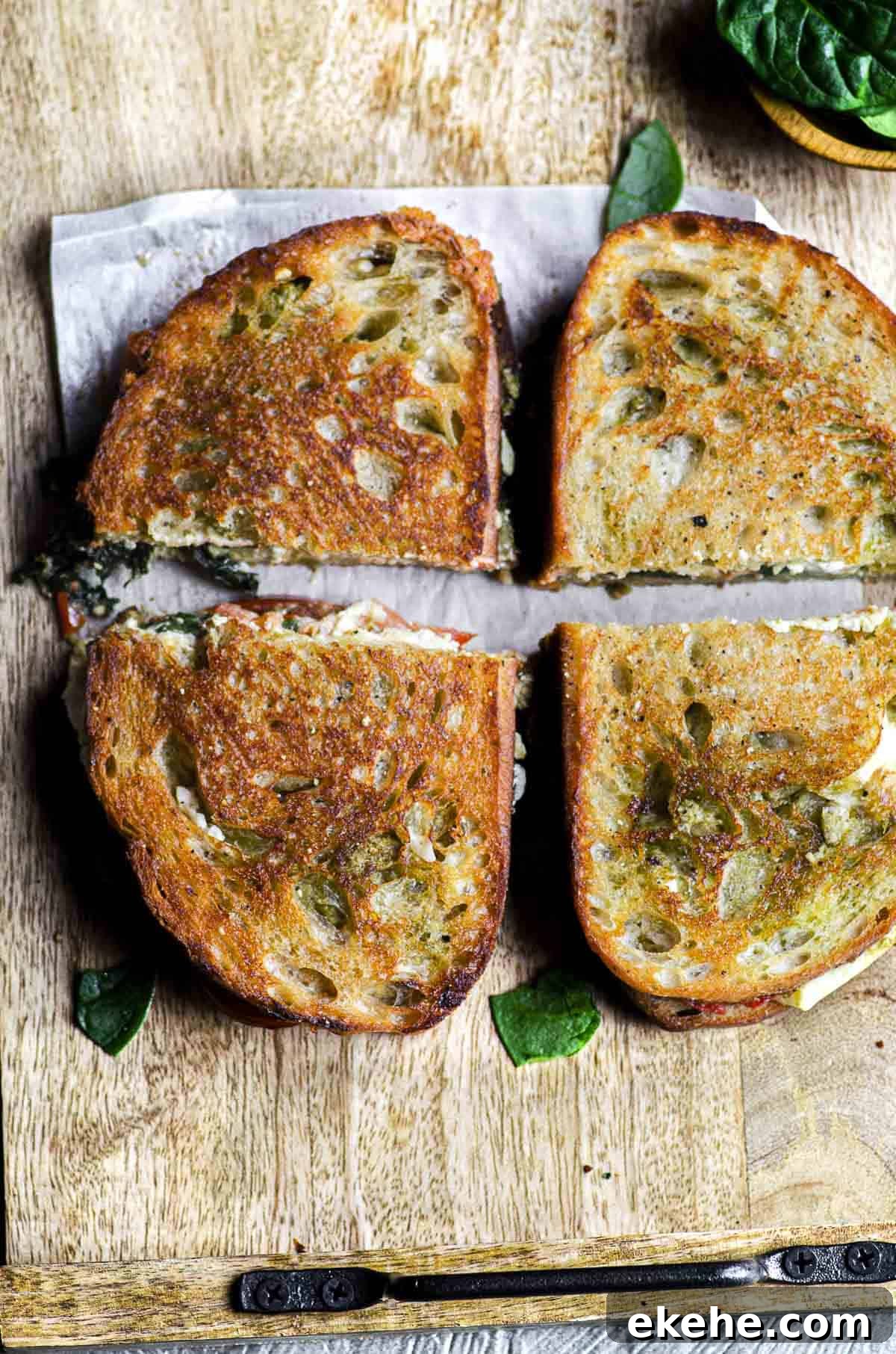 Two grilled cheese sandwiches with feta cheese, tomatoes, and spinach cut into four pieces