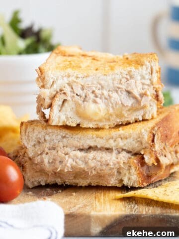 Air fryer tuna melt sandwich on a wooden board with salad and crisps.