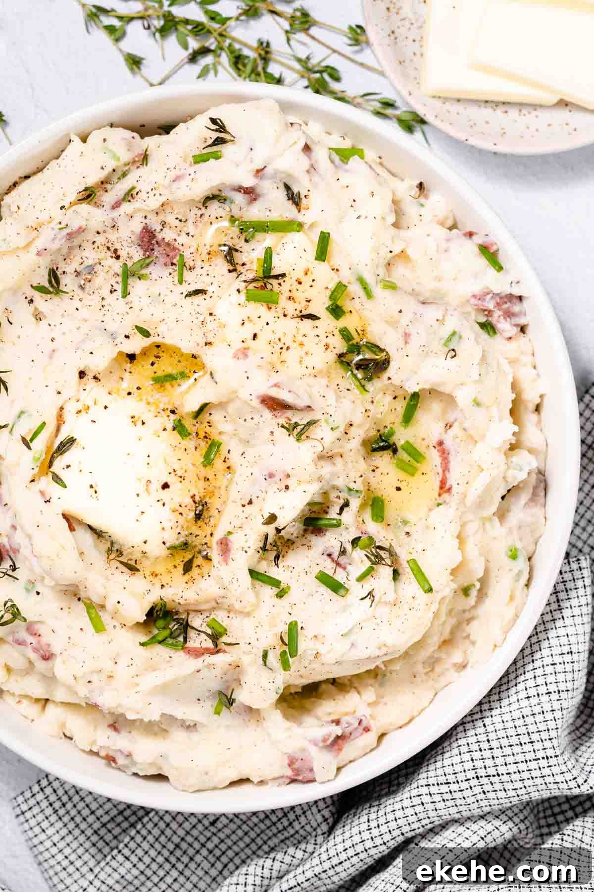 red skin mashed potatoes in bowl with herbs and butter on top.