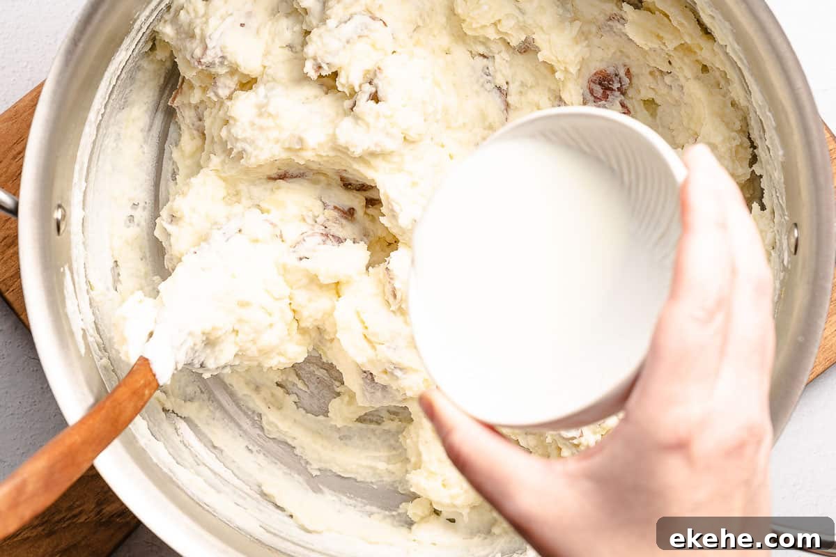 milk being poured into pot of mashed potatoes
