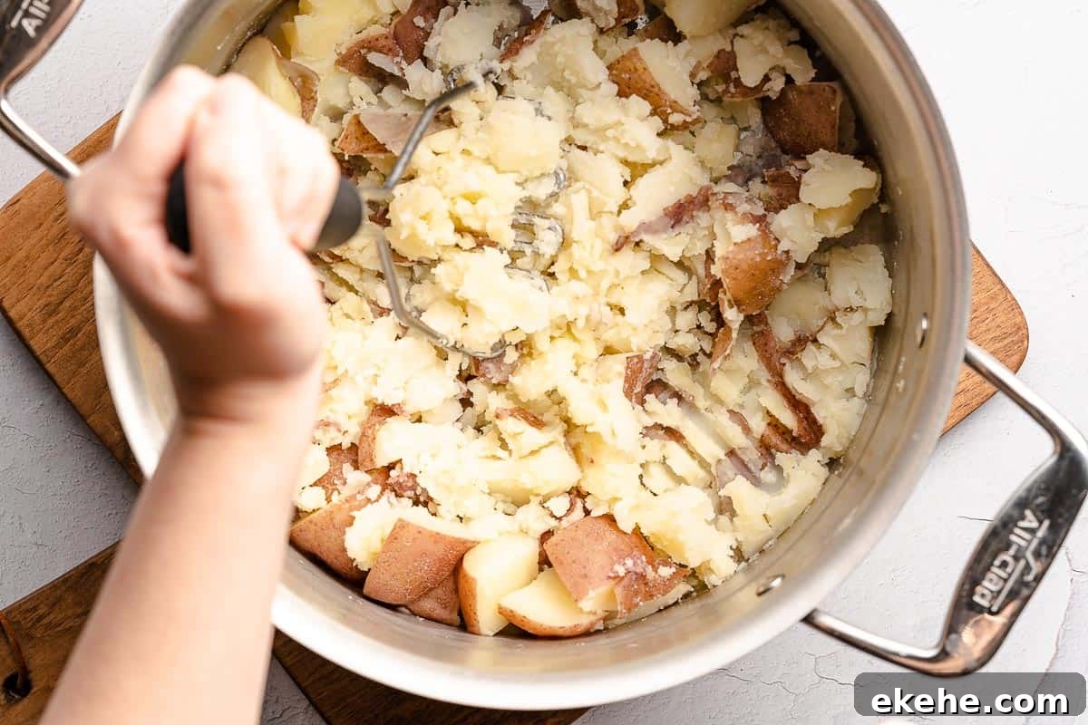 cooked potato chunks being mashed with potato masher in pot