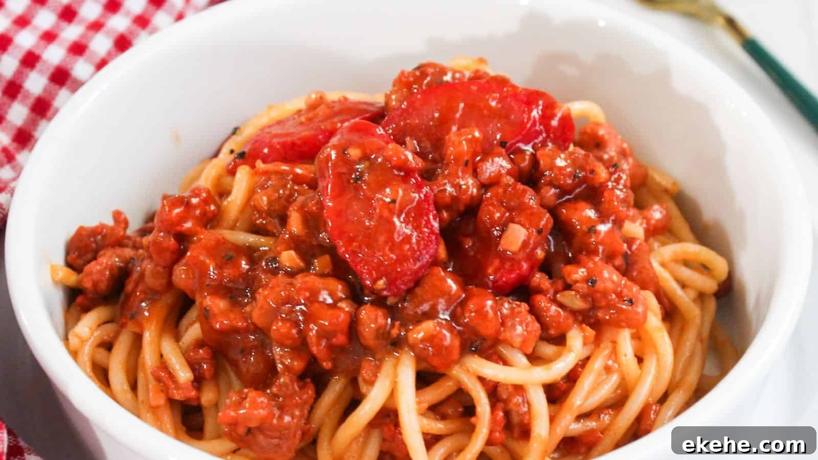 A bowl of spaghetti topped with a rich meat sauce placed on a red and white checkered tablecloth.