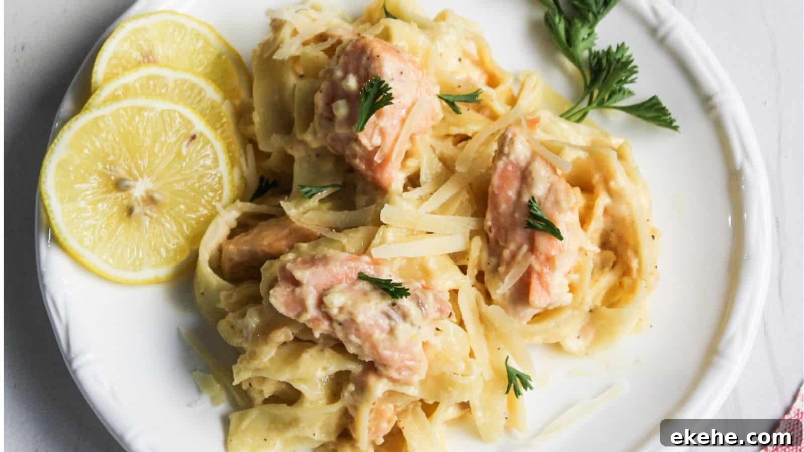 Salmon pasta Alfredo served on a white plate with lemon.